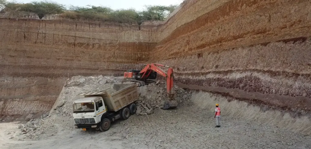 industrial excavator loading raw China clay (kaolin) into a white dump truck at an open-pit mining site with layered earth walls